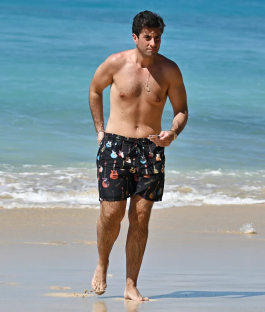 Man walking on a beach in guitar-print swim shorts.