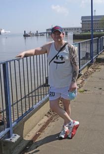 Man with tattoos standing by a railing on a pier.