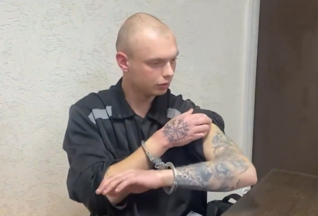 A handcuffed man with tattoos showing a Vegvisir on his hand.