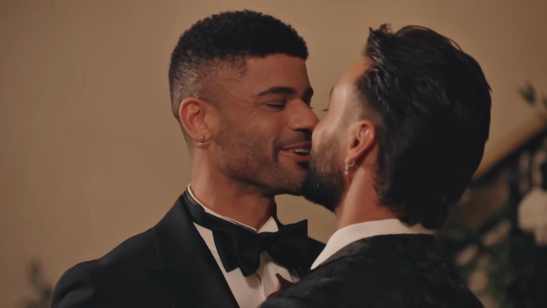 Two men in tuxedos, one kissing the other on the cheek, at their wedding.