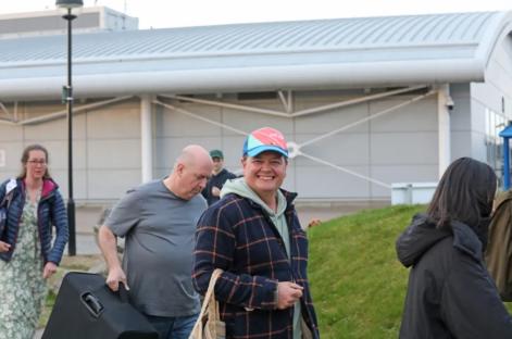 A man smiling while carrying a bag, with other people in the background.