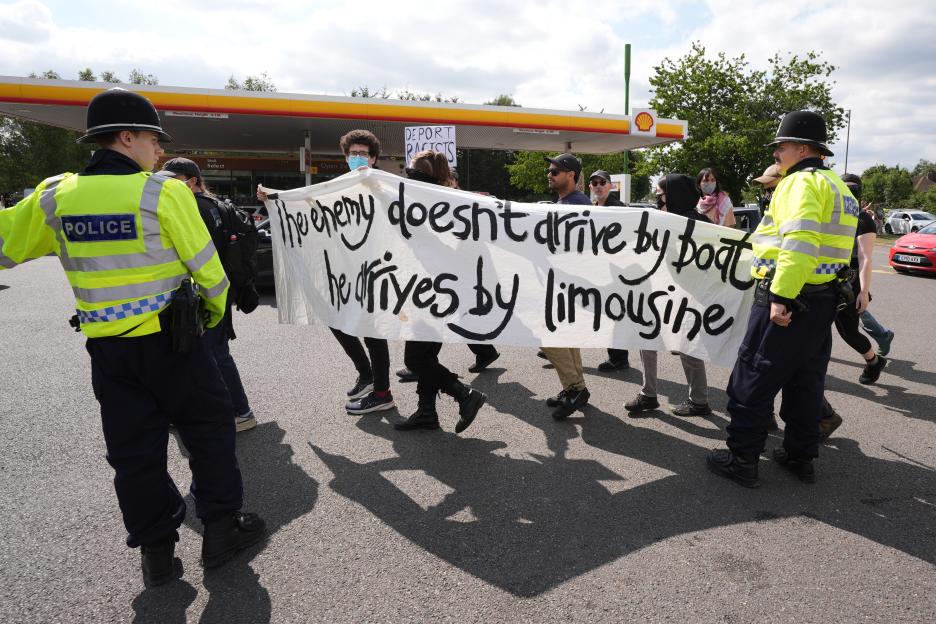Protestors carrying a banner that reads, "The enemy doesn't arrive by boat, he arrives by limousine," are monitored by police.