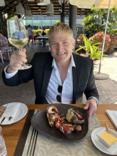 Man in a suit enjoying a grilled lobster meal with a glass of white wine in the Canary Islands.