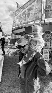 Woman carrying toddler at a funfair.