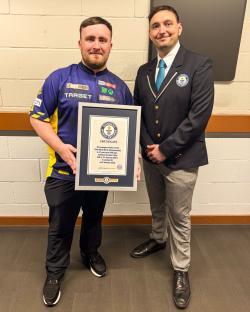 Two men holding a Guinness World Records certificate for the youngest winner of the PDC World Darts Championship.
