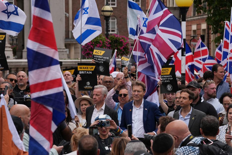 Former Conservative cabinet minister Michael Gove and Reform UK Deputy Leader Richard Tice marching against antisemitism, holding signs with slogans like "Wake Up Britain" and "Extremists won't stop at Jews" and surrounded by people holding British and Israeli flags.