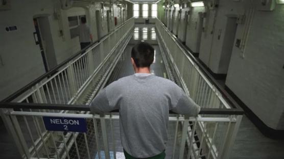 A prisoner stands on a landing overlooking a prison corridor.
