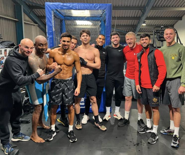 Group photo of men in a gym, some shirtless.