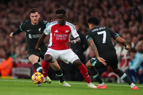 Bukayo Saka of Arsenal pressured by Liverpool players during a soccer match.
