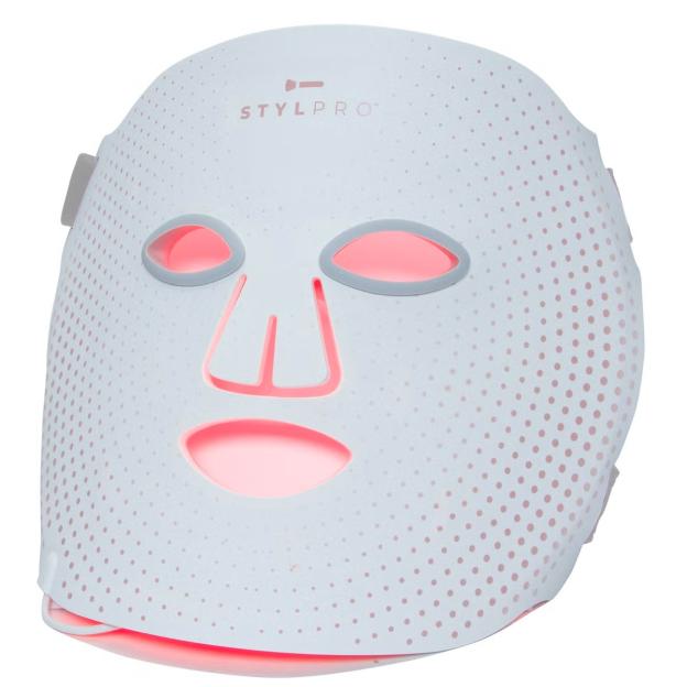 A white Stylpro LED face mask with red light emanating from the eye, nose, and mouth cutouts, and from the small dots covering the mask.
