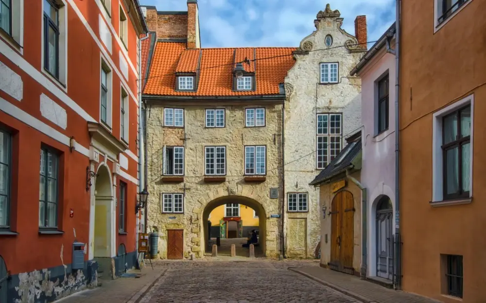 Three historic buildings in Riga, Latvia, with a cobblestone street in the foreground.