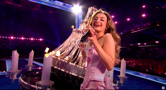 Singer performing on stage with a large chandelier.