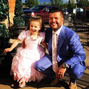 Man in suit crouching with a girl in a pink dress.