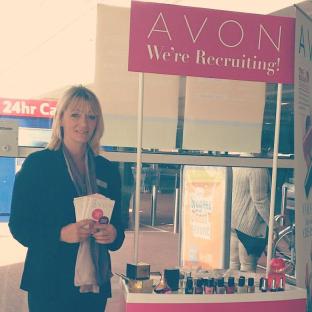 Woman at Avon recruiting booth holding brochures.