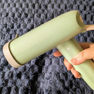 A hand holding a light green clothes steamer.