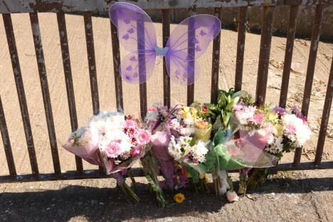Floral tributes and a pair of purple fairy wings left at a fence.