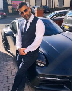 Man in suit leaning against a black sports car.