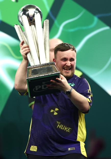 Luke Littler holding up a trophy after winning a darts championship.