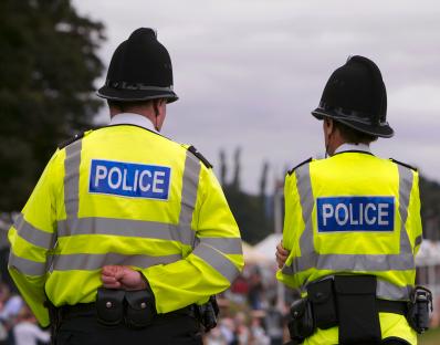 Two British police officers in uniform stand facing away from the camera.