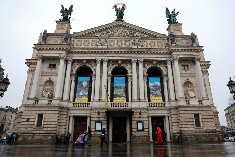 People walk past the Lviv National Opera house, decorated with large banners honoring Ukrainian heroes, on a rainy day.