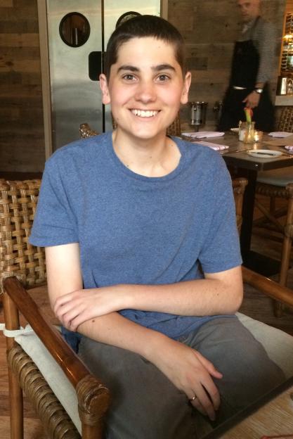 A teenage boy smiles while sitting in a wicker chair at a restaurant.