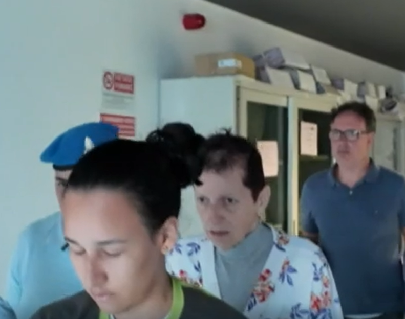 A person in a floral shirt being escorted by police officers.