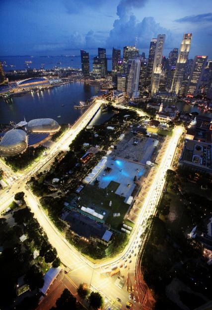 The Marina Bay Circuit street course in Singapore as seen from a hotel at dusk, with city lights and surrounding buildings.