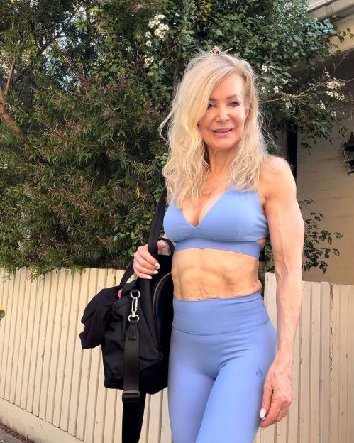 A muscular older woman in a light blue sports bra and leggings carries a black gym bag.