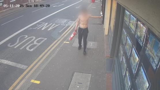 Surveillance image of a shirtless man carrying a fire extinguisher.