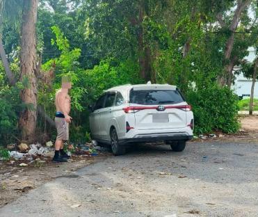 A shirtless man stands near a white Toyota Veloz in a parking lot.