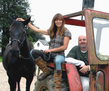 Woman and man sitting on a tractor with a horse.