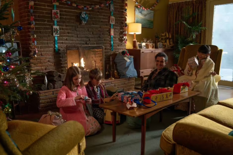 Family opening Christmas presents by a fireplace.