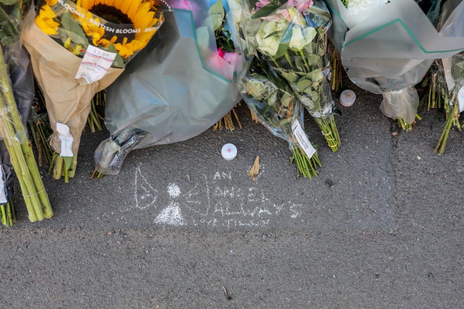 Floral tributes and chalk messages at a roadside memorial.