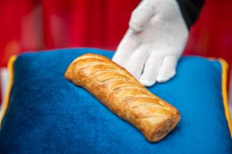 A Greggs sausage roll on a blue cushion.