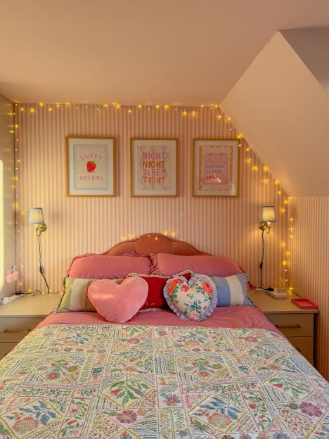 Pink bedroom with floral bedding, fairy lights, and framed prints.
