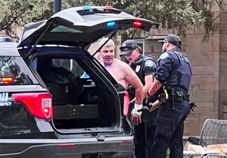 Police officers detaining a shirtless suspect.