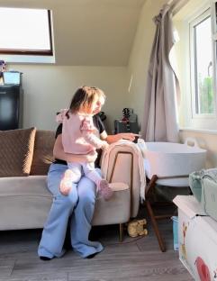 A mother holding her toddler daughter near a baby bassinet.