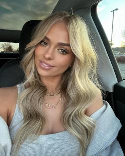 Woman with long blonde hair and gold necklaces in a car.