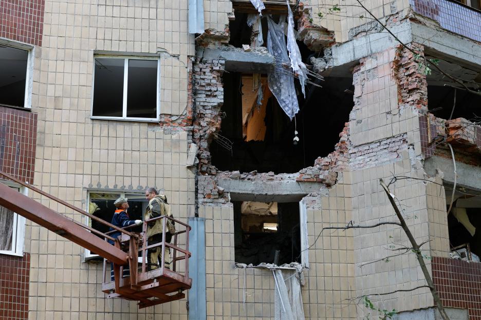 Workers removing debris from a damaged apartment building.
