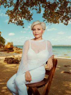 Woman in white sitting on a bench by the beach.
