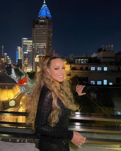 Mariah Carey on a rooftop at night, overlooking a city skyline.