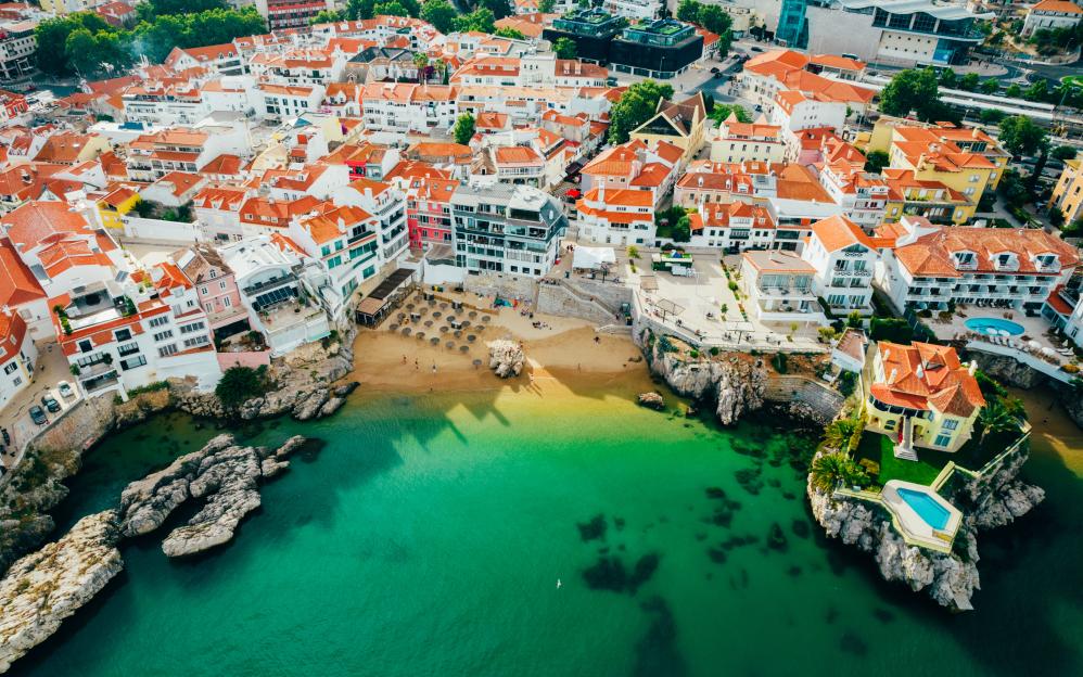 Drone aerial view of Praia da Rainha and historic city centre of Cascais, Portugal.