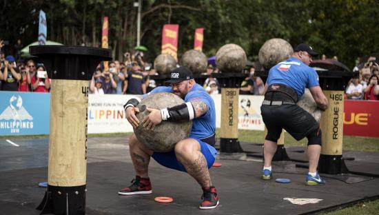 Two strongmen lifting heavy concrete spheres in a competition.