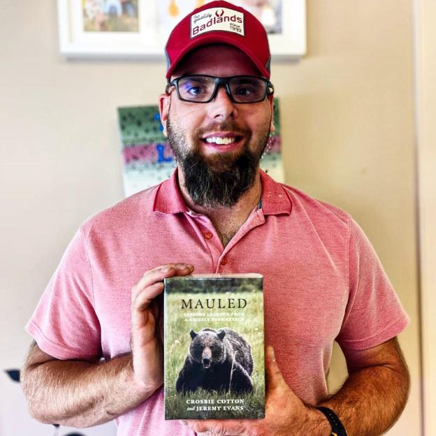 Man holding a copy of "Mauled: Lessons Learned From a Grizzly Bear Attack."