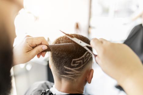 Hairdresser cutting a man's hair with a design shaved into the back of his head.