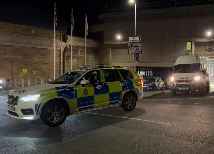 A prison van leaves Wakefield prison, with a police car in the foreground.