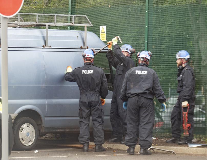 Police officers examining a van used to ram a fence.