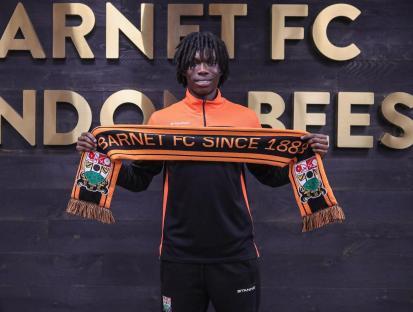A person holding a Barnet FC scarf in front of a sign that says