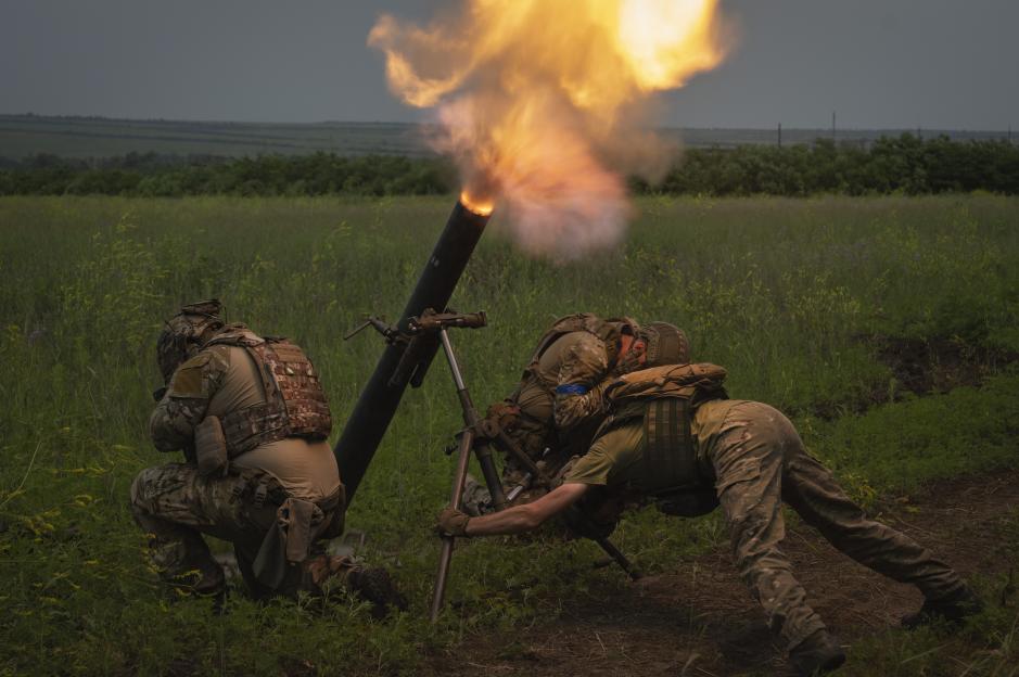 Two Ukrainian soldiers firing a mortar with a bright flash of light and smoke.