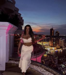 Woman in white outfit on balcony overlooking city at night.